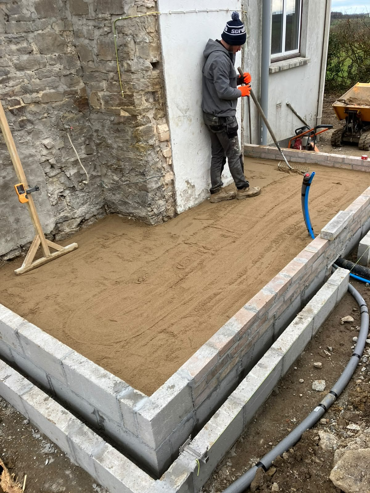 Levelling the sand base inside new blockwork foundations with drainage runs laid alongside